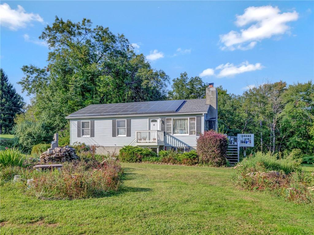 View of front of property featuring a front lawn, a wooden deck, and solar panels