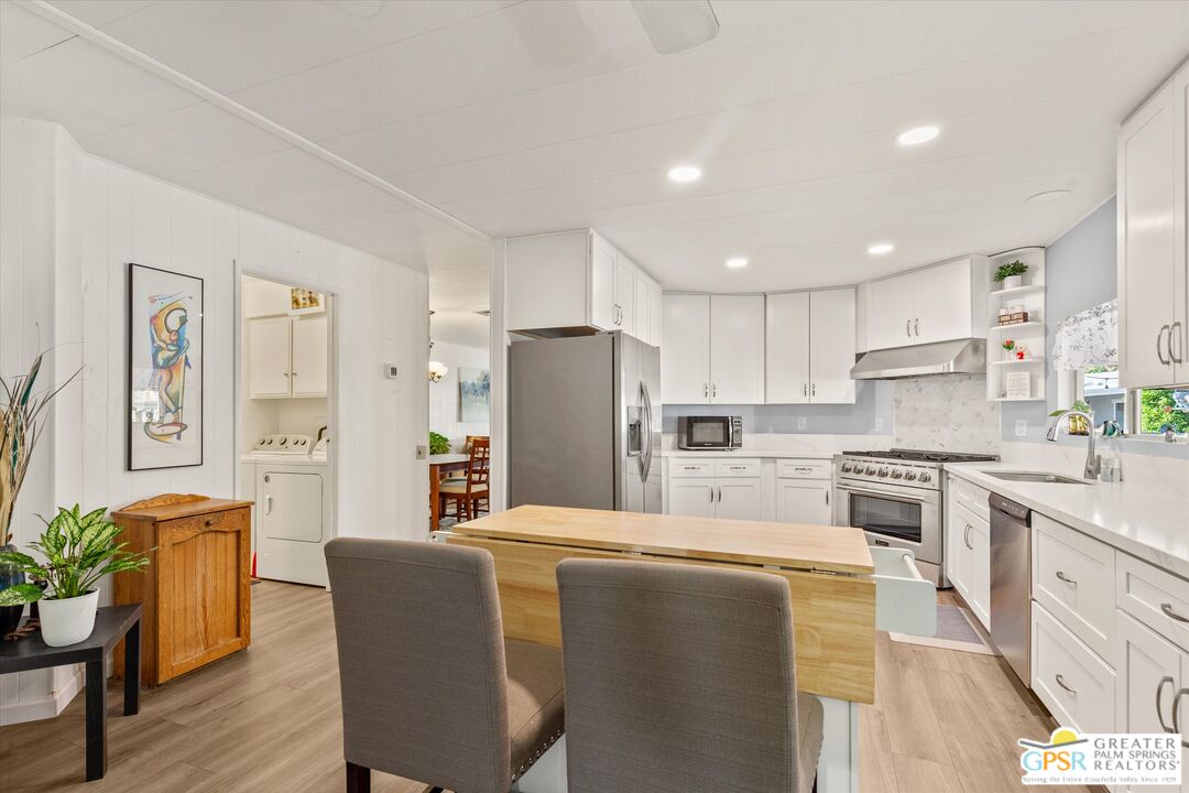 a kitchen with stainless steel appliances kitchen island granite countertop a refrigerator a stove a sink a dining table and chairs with wooden floor