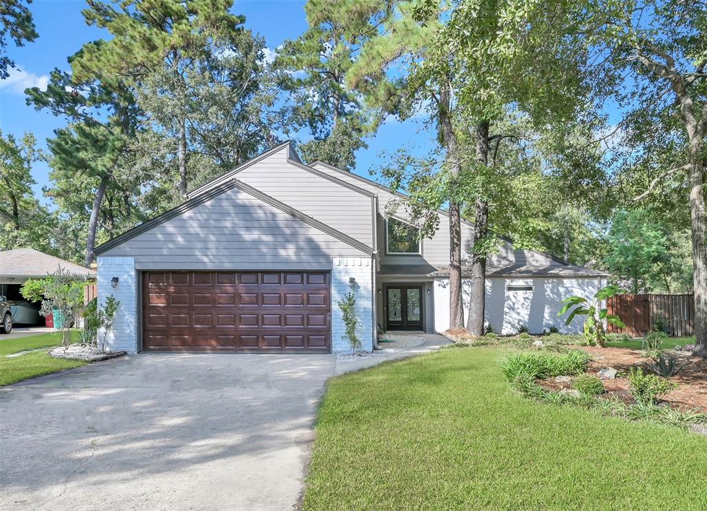 Two-story home featuring a large attached garage, a freshly manicured lawn, and mature trees providing shade and privacy. The exterior has a clean, traditional look with brick accents.