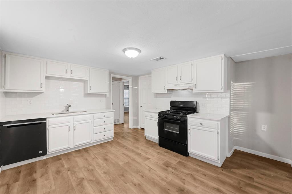 Kitchen featuring stainless steel dishwasher, white cabinets, light wood-type flooring, and black gas range oven