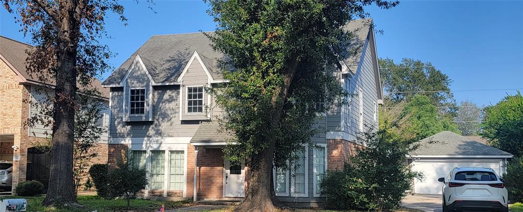 This is a charming two-story home with a classic design, featuring a combination of brick and siding. It has large front windows, a gabled roof, and a spacious driveway leading to a detached garage. The property is surrounded by mature trees, providing shade and privacy.