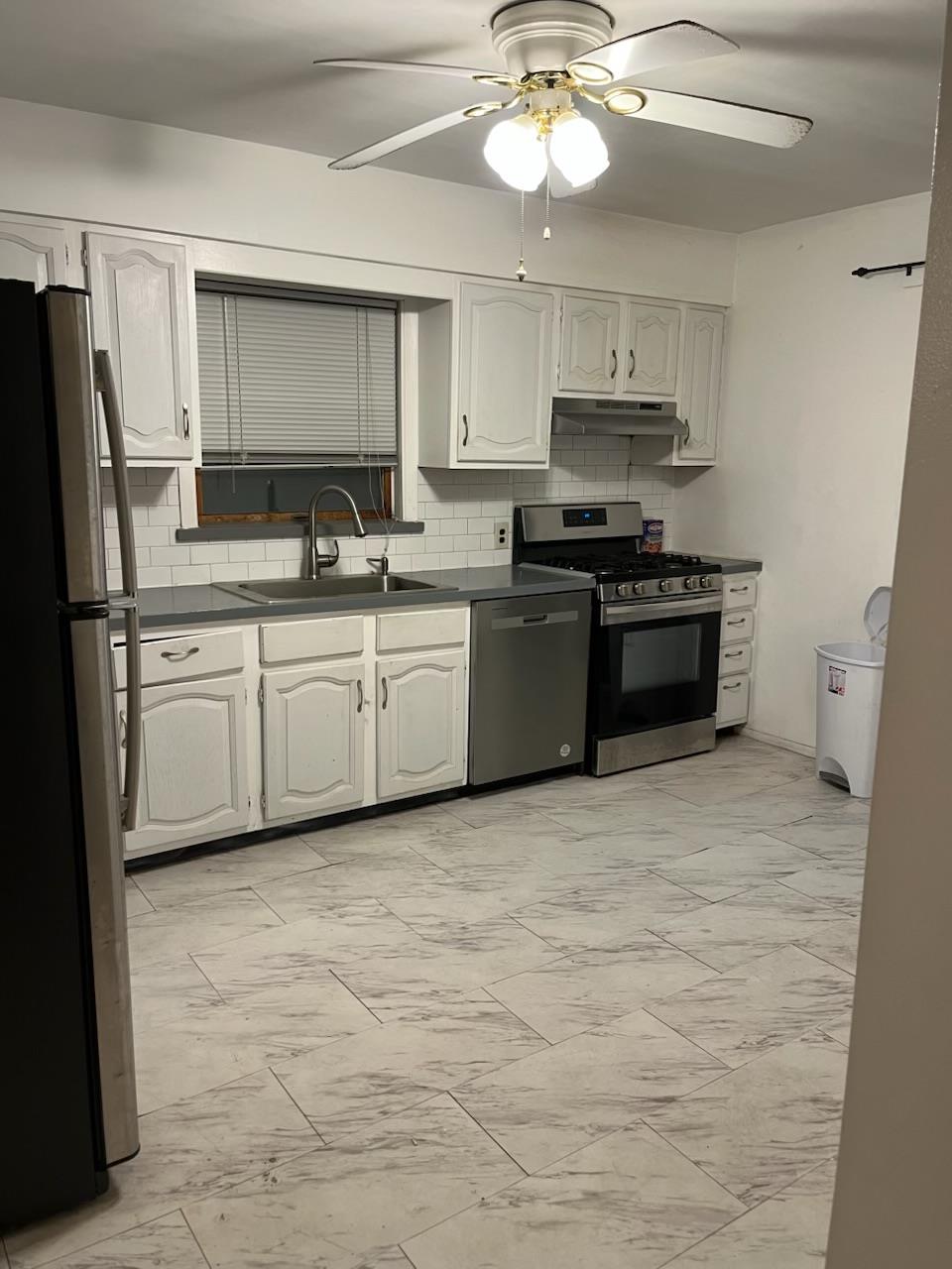 Kitchen featuring backsplash, stainless steel appliances, ceiling fan, sink, and white cabinetry