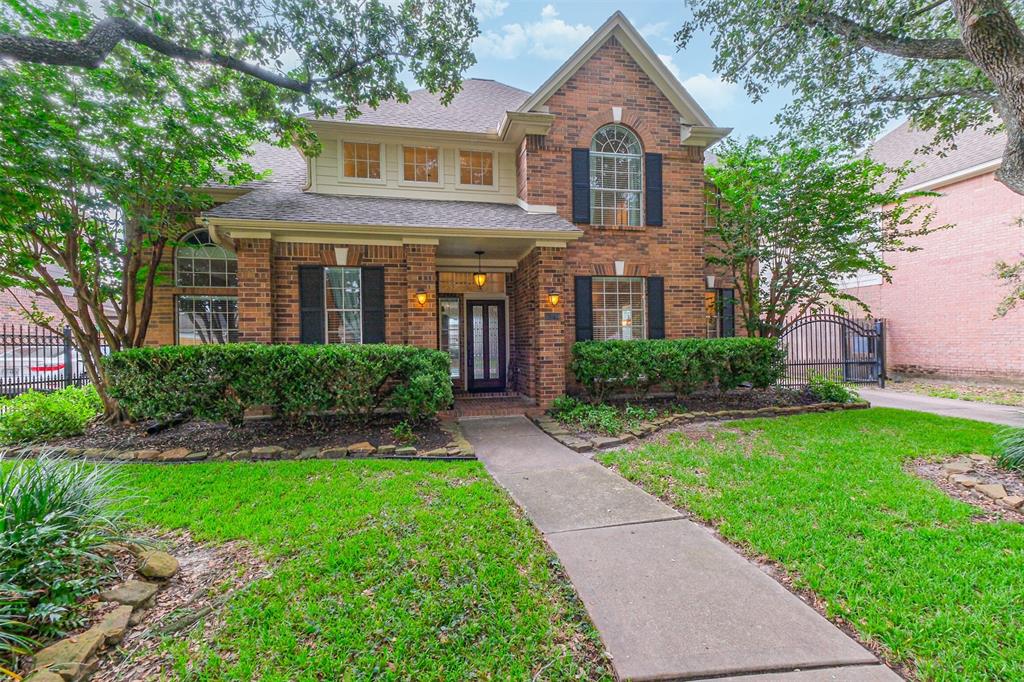 Traditional two-story brick home with a well-maintained lawn and mature landscaping. Offers a cozy front porch and a gated driveway for added privacy.