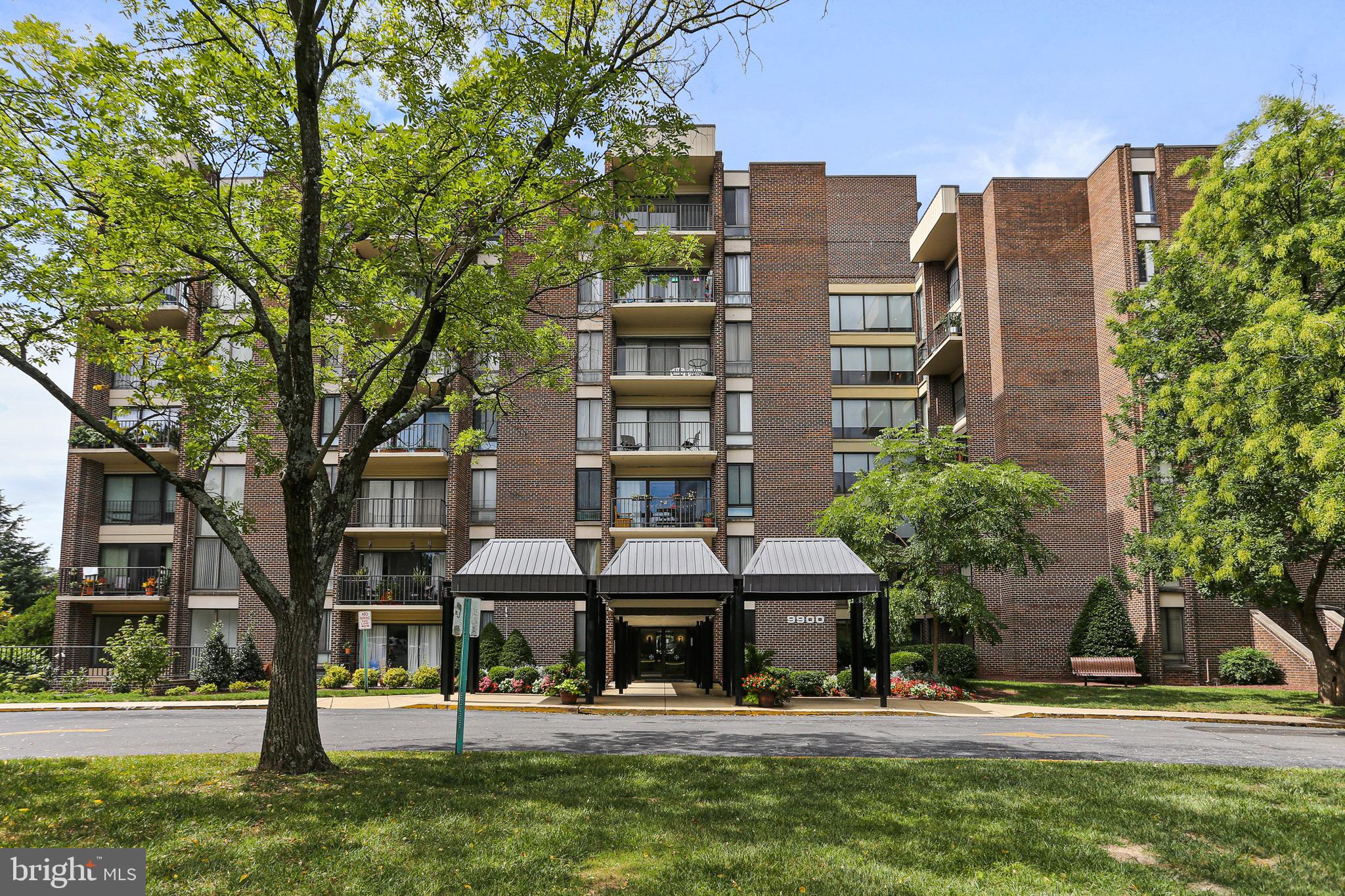 a front view of a building with a garden and trees