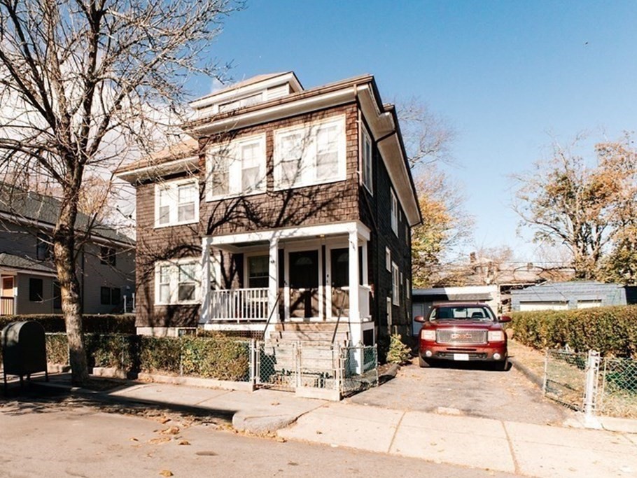 a view of a house with a large tree and cars parked