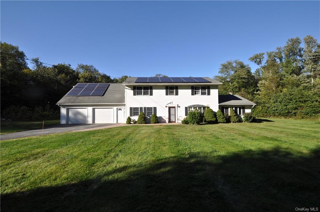 Colonial home featuring a garage, a  a manicured front lawn, and solar panels