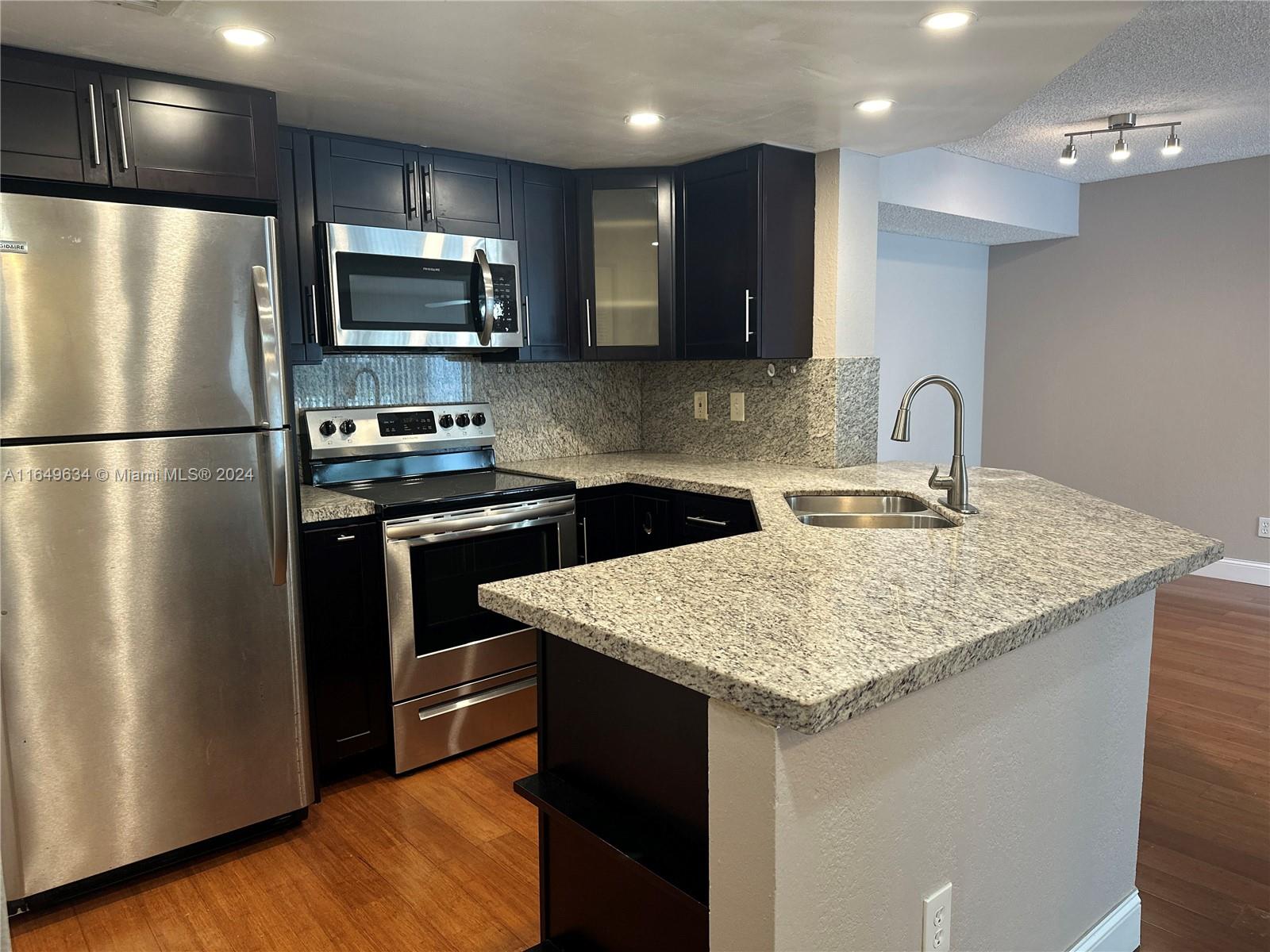 a kitchen with stainless steel appliances granite countertop a refrigerator a sink a stove a microwave and cabinets