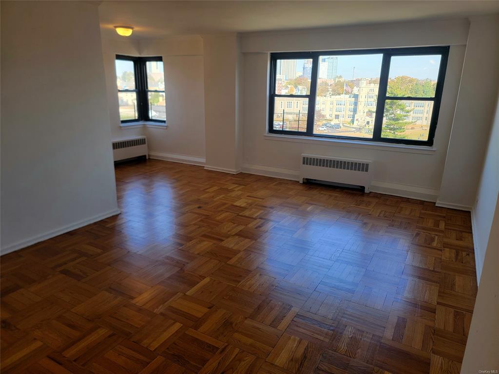 Empty room featuring dark parquet floors, plenty of natural light, and radiator