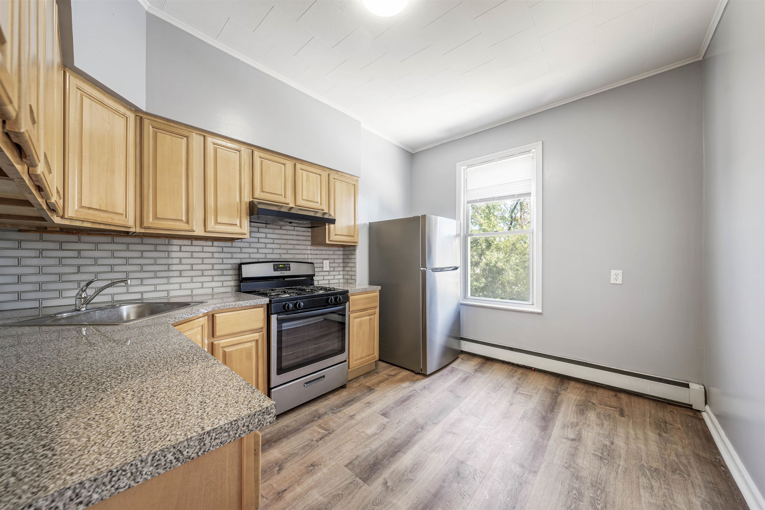 a kitchen with granite countertop wooden floors stainless steel appliances a sink and a window