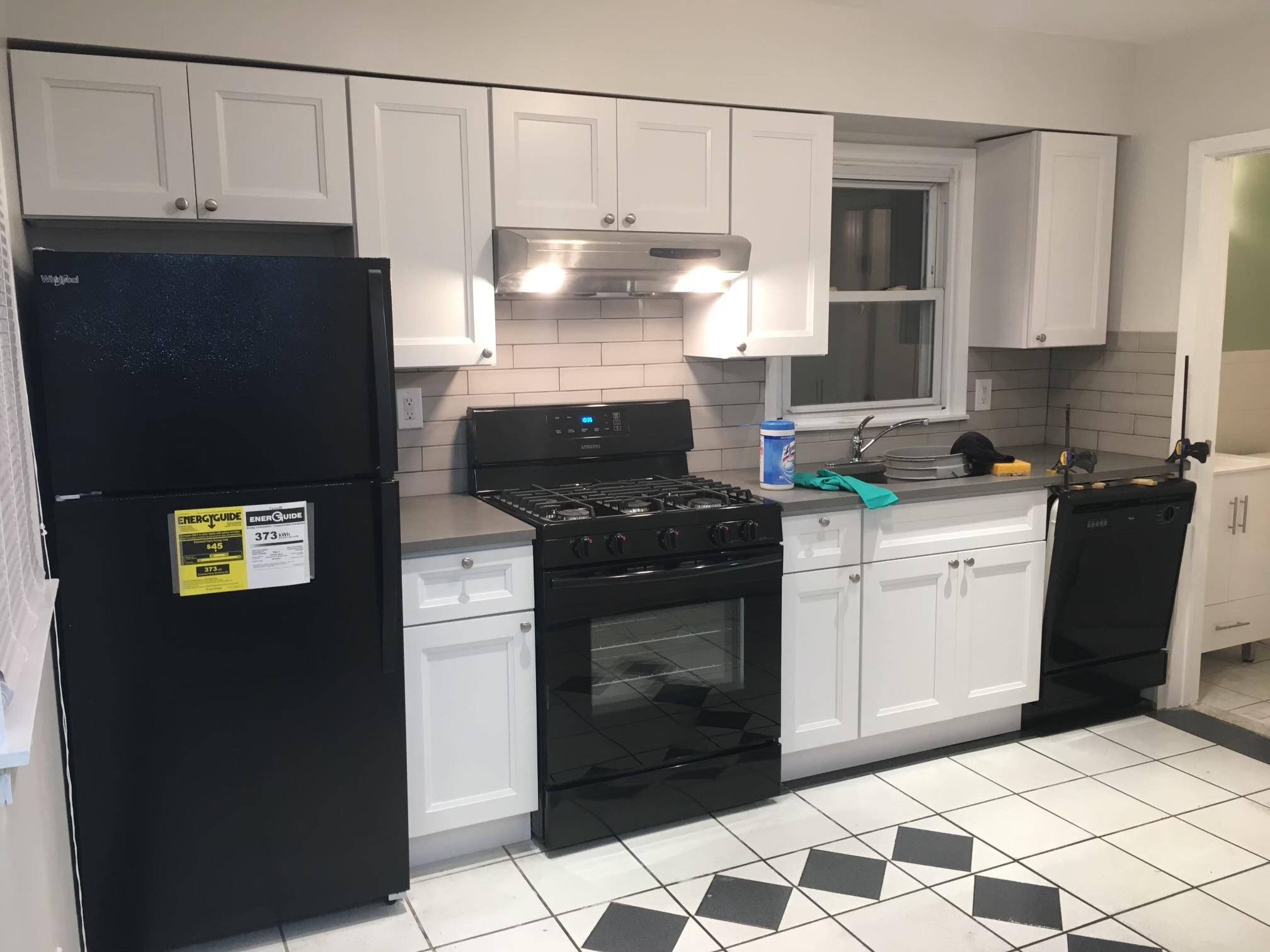 Kitchen featuring decorative backsplash, white cabinetry, light tile patterned flooring, and black appliances