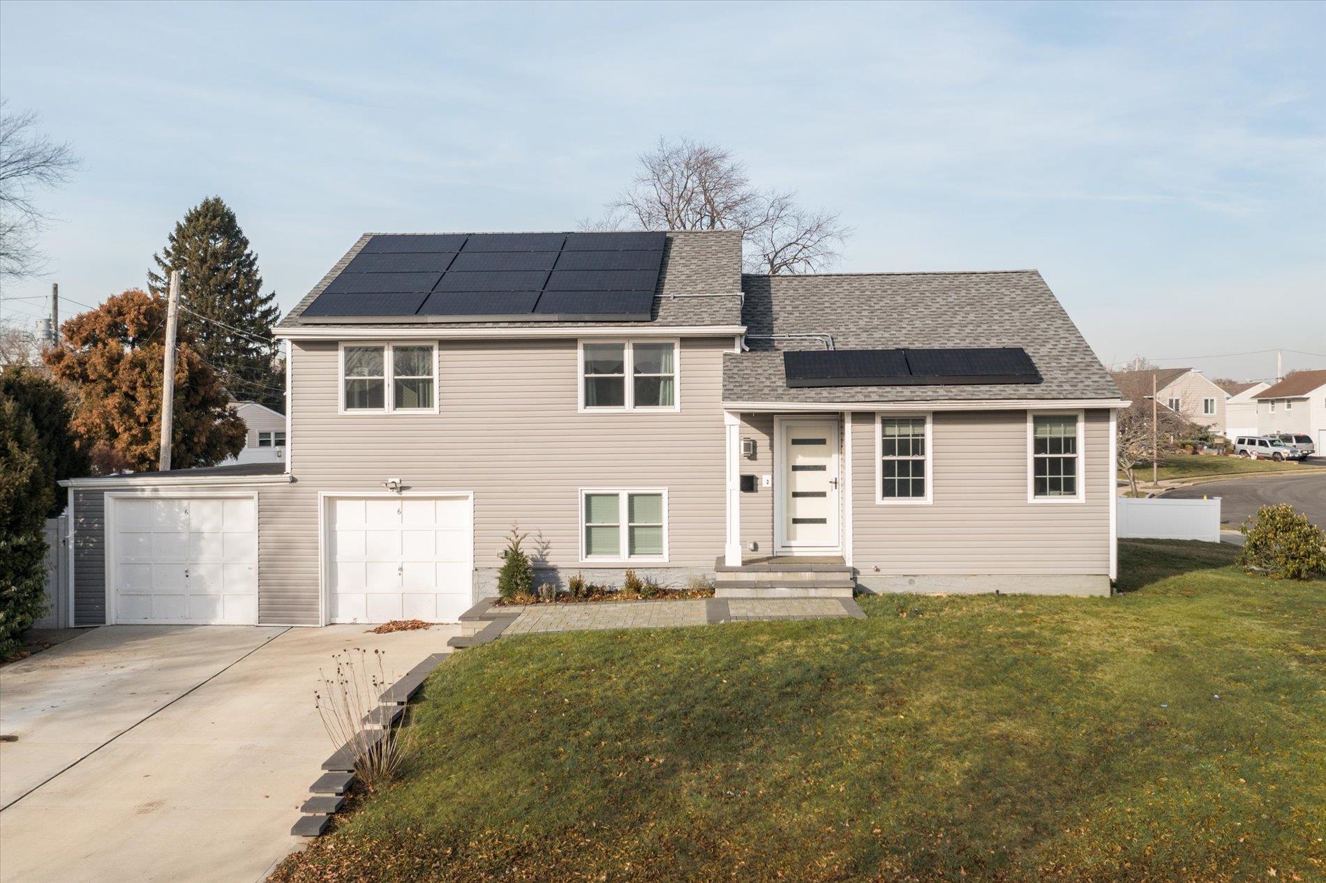 Tri-level home featuring a front lawn, a garage, and solar panels