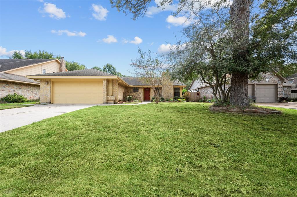 Single-story house with a well-manicured lawn and a large tree in the yard. The home features a two-car garage and a brick facade, nestled in a peaceful, suburban neighborhood.