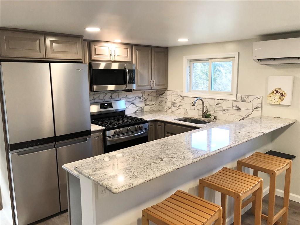 Kitchen featuring  kitchen peninsula, sink, appliances with stainless steel finishes, and a wall mounted air conditioner