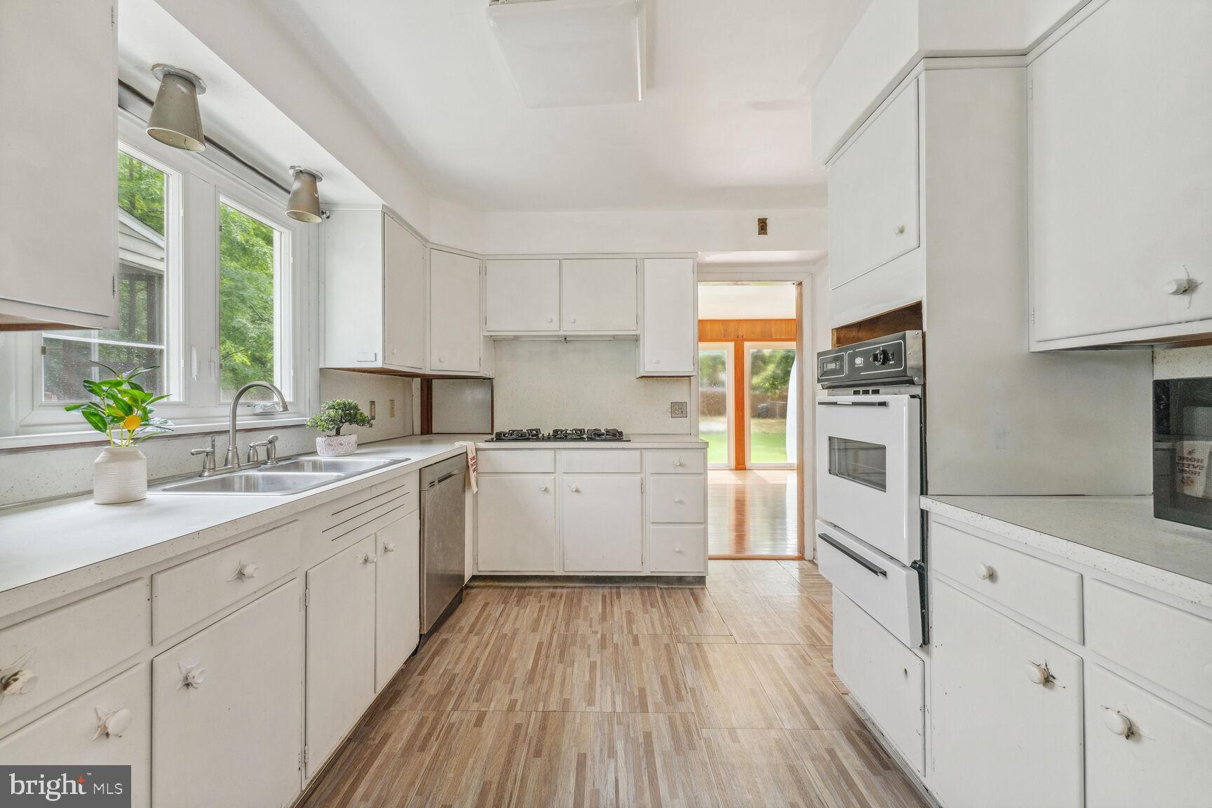 a kitchen with white cabinets a sink dishwasher and a stove with wooden floor