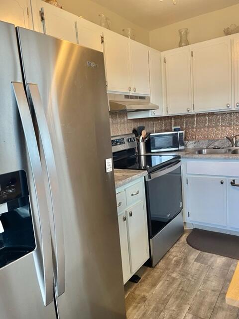 a kitchen with stainless steel appliances a refrigerator a sink and white cabinets