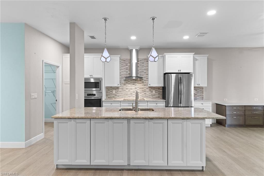 Kitchen featuring wall chimney range hood, light hardwood / wood-style flooring, an island with sink, stainless steel appliances, and backsplash