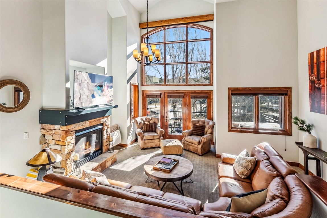 Living room featuring a stone fireplace, a chandelier, and a high ceiling