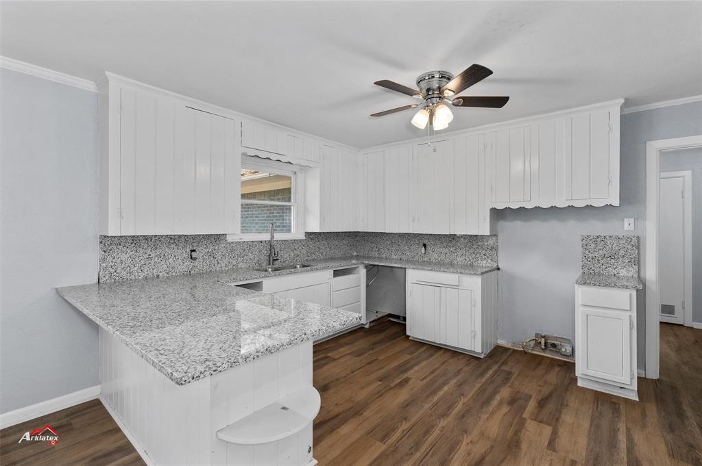 a kitchen with a sink dishwasher a stove and white cabinets with wooden floor