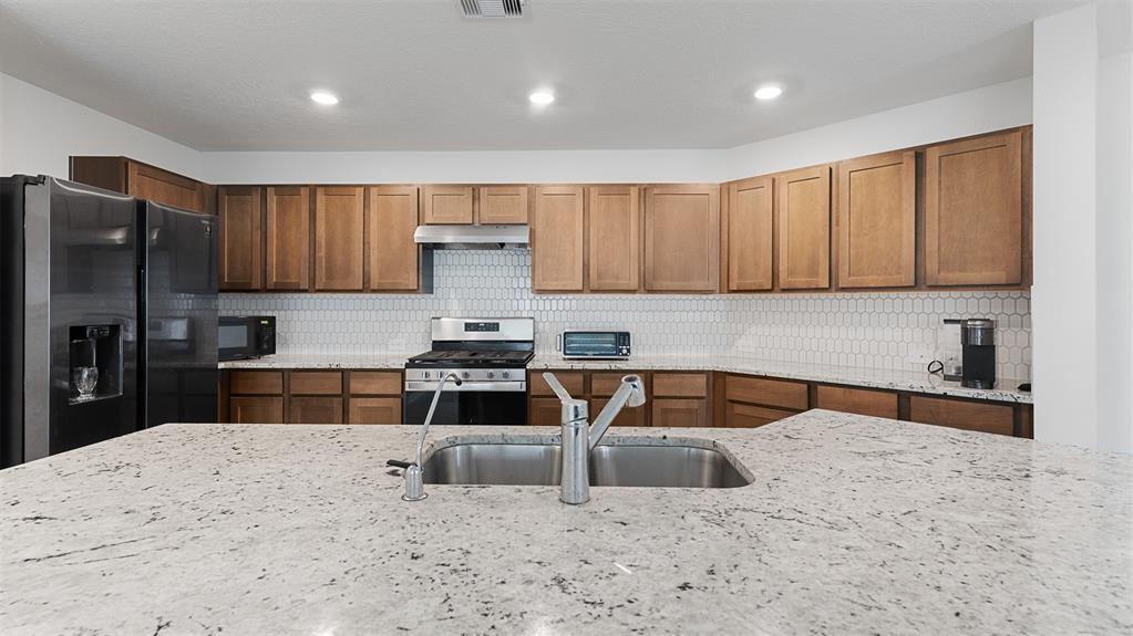 a kitchen with granite countertop a sink a stove a refrigerator and cabinets