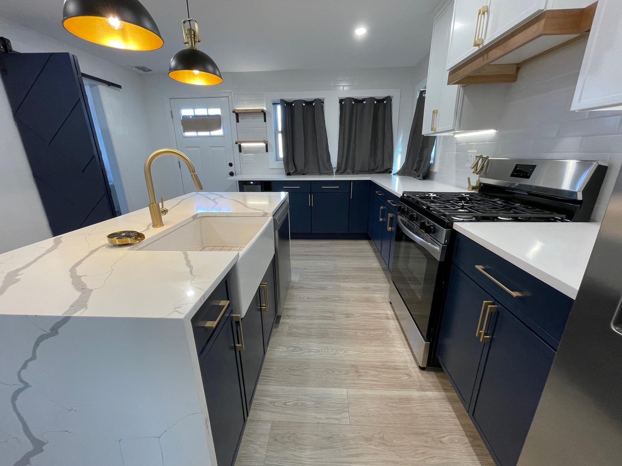 Kitchen with pendant lighting, white cabinets, blue cabinetry, an island with sink, and appliances with stainless steel finishes