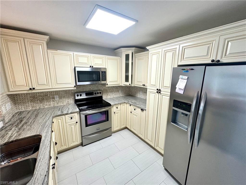 Kitchen with cream cabinetry, sink, stainless steel appliances, and tasteful backsplash