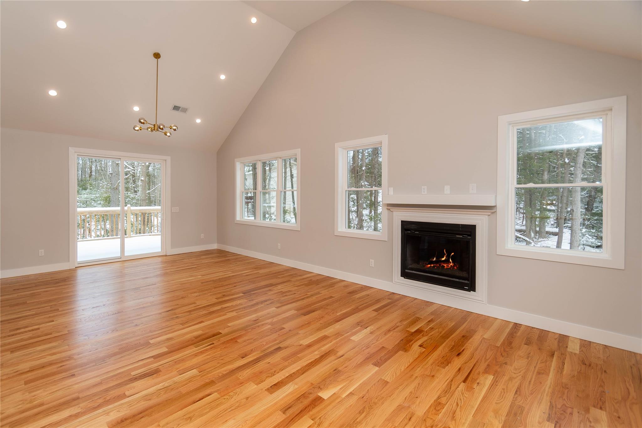 Living/dining room w lots of lights. Large windows for extra natural light, hardwood floors, and high vaulted ceiling. Slider to deck and fireplace.