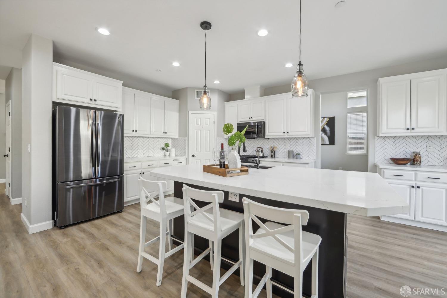 a kitchen with stainless steel appliances kitchen island granite countertop a refrigerator a stove a sink a dining table and chairs with wooden floor