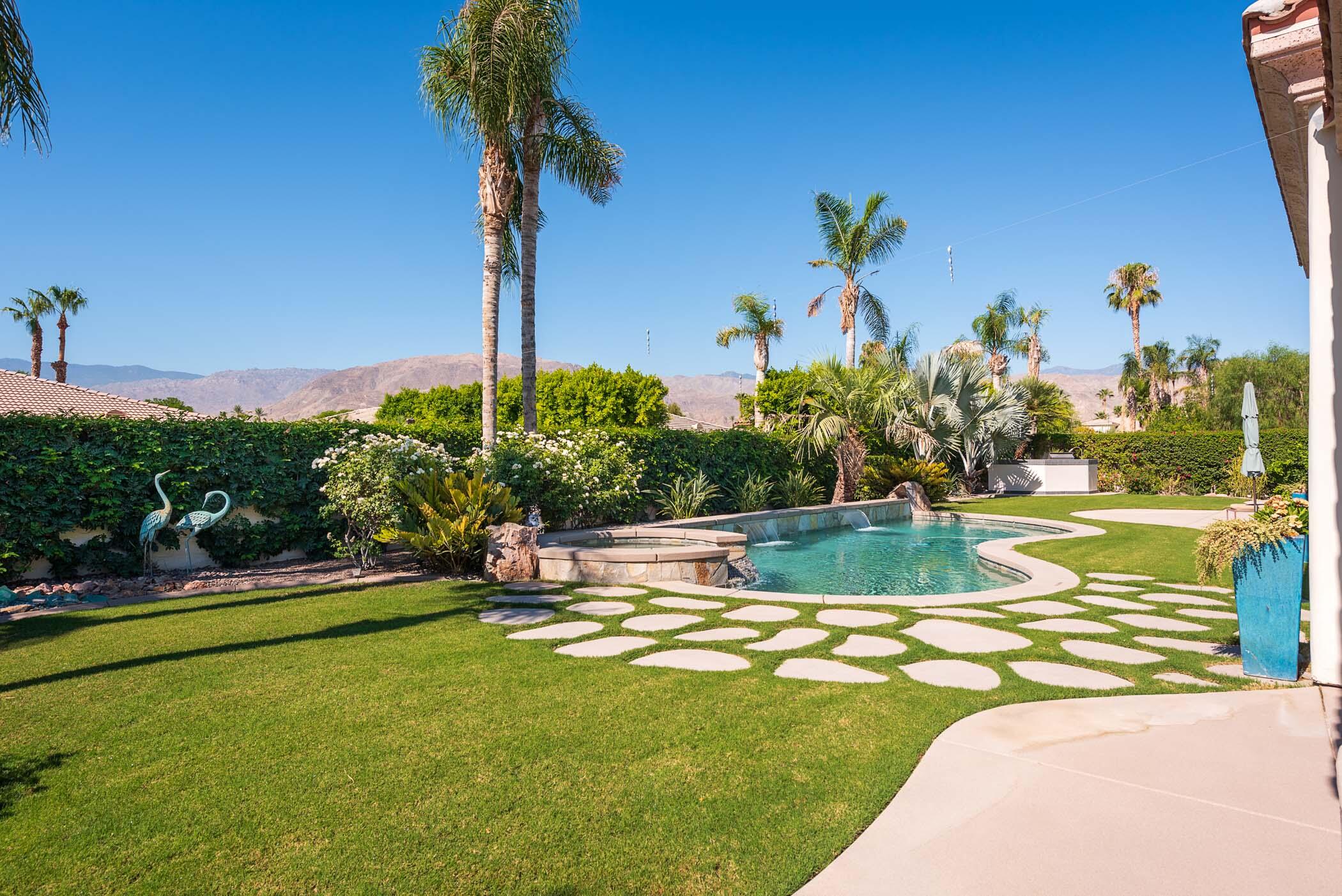 a view of a swimming pool with a yard and palm trees