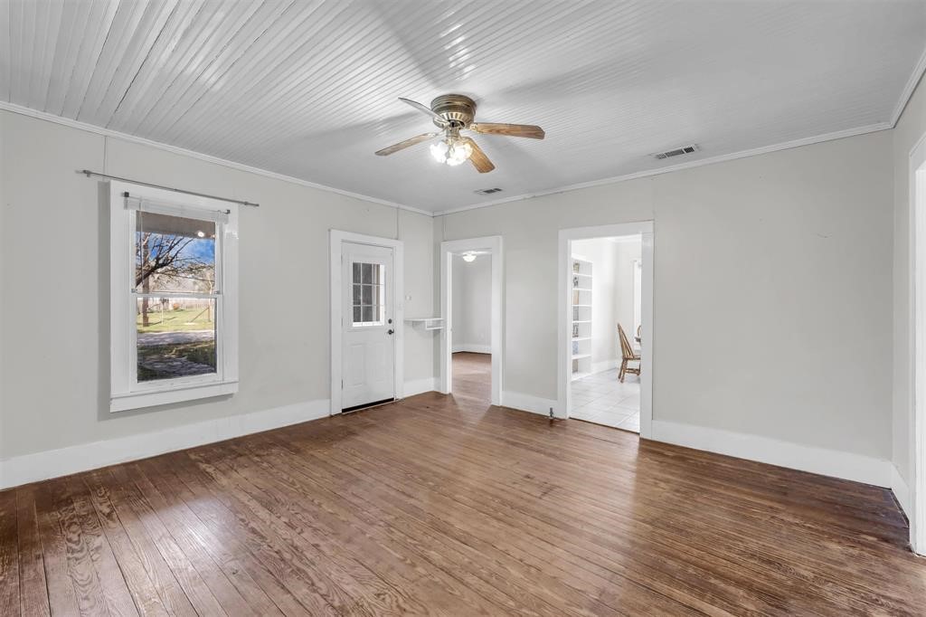 a view of an empty room with wooden floor and a ceiling fan