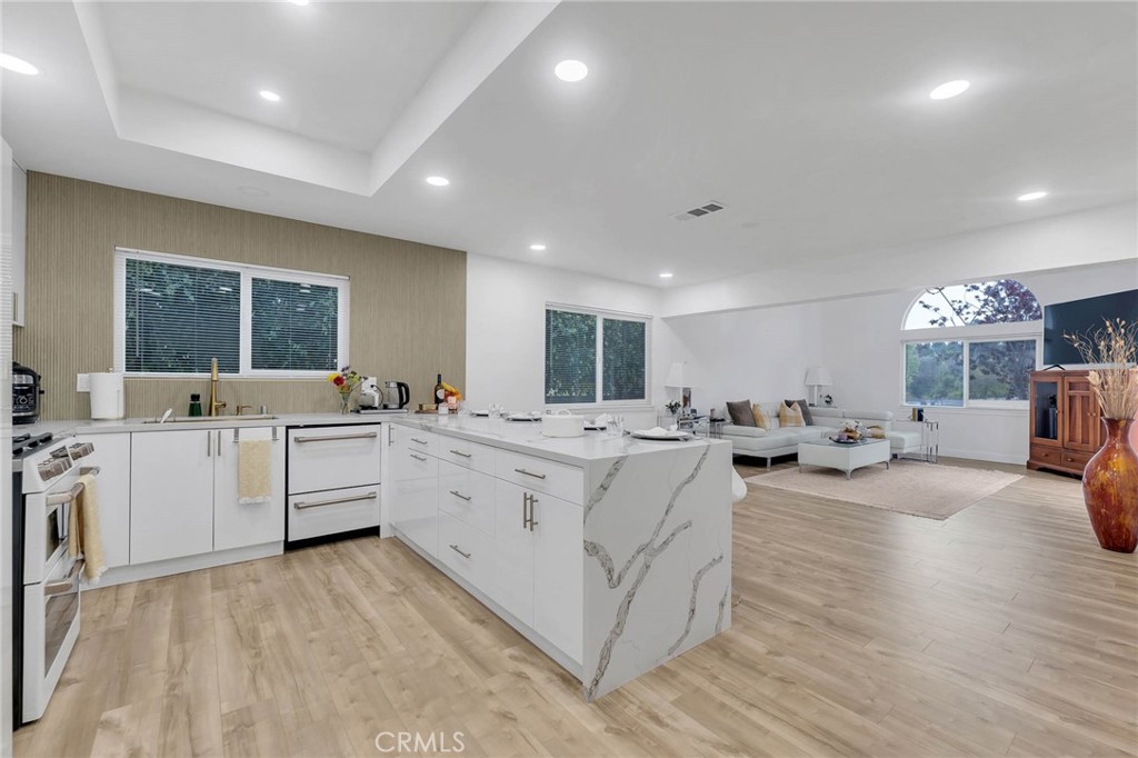 a large white kitchen with cabinets a sink a window and chairs