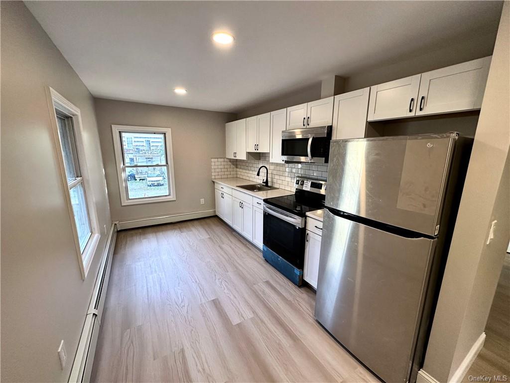 Kitchen featuring white cabinets, sink, backsplash, light wood-type flooring, and appliances with stainless steel finishes