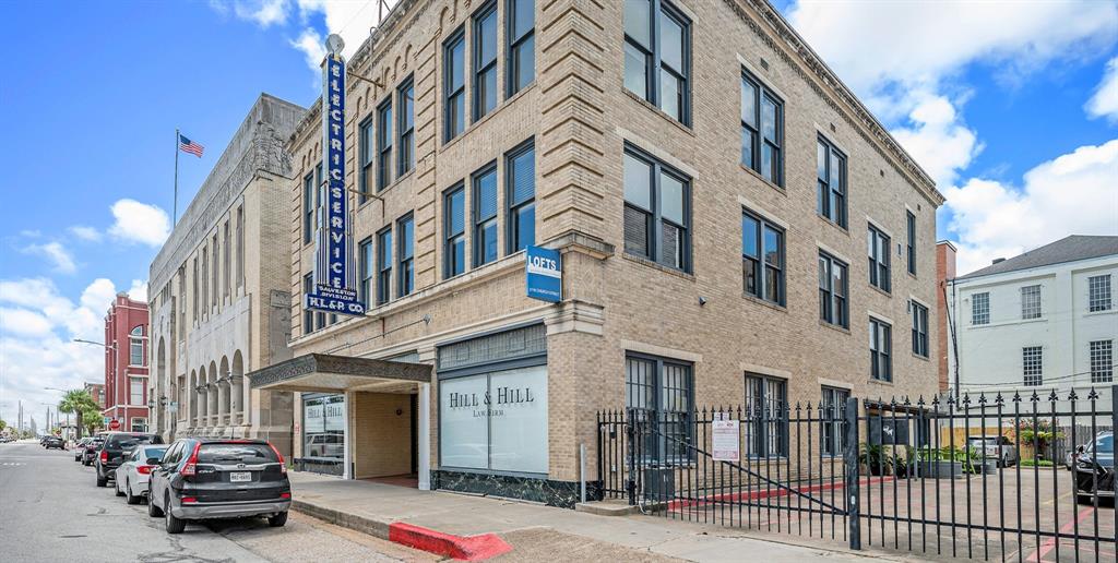 This is a street-level view of the historic multi-story Galveston Electric Company building in an urban setting with a commercial space on the ground floor, featuring classic architecture and a prominent location. The area includes on-street parking and is within walking distance of other city amenities and businesses.