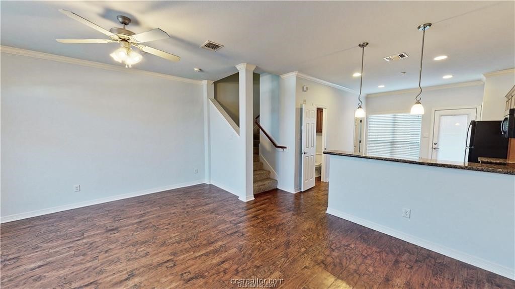 a view of an empty room with wooden floor and a ceiling fan