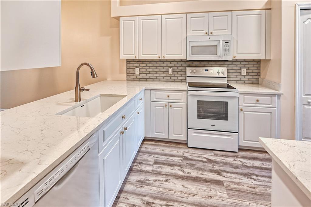 Kitchen featuring light stone counters, light hardwood / wood-style floors, sink, white cabinetry, and white appliances