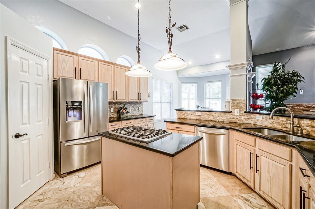 This is a spacious and modern kitchen featuring stainless steel appliances, a gas stove on the island, ample cabinet space, and granite countertops. The room is well-lit with natural light from the large windows and stylish pendant lighting.