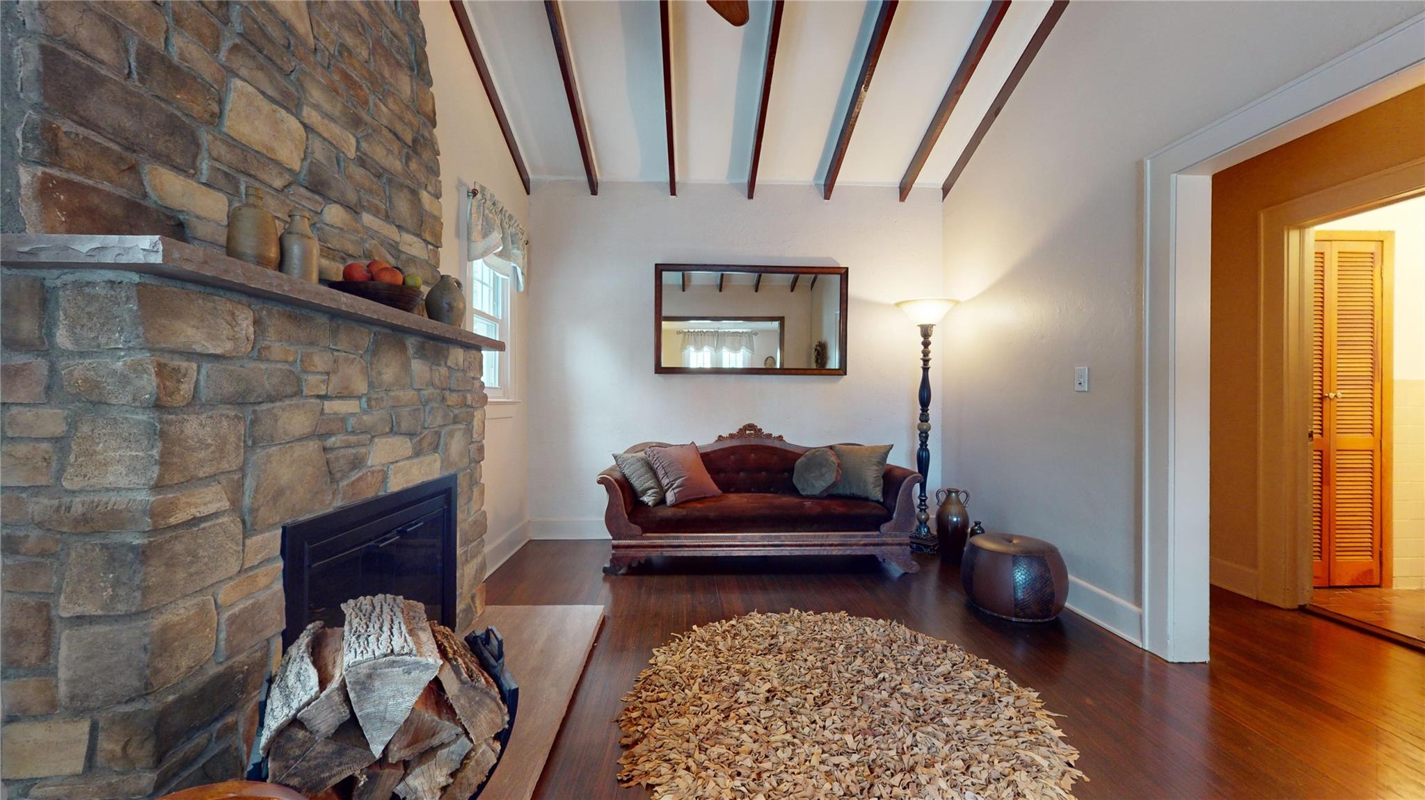 Living room with lofted ceiling with beams, a fireplace, and dark wood-type flooring