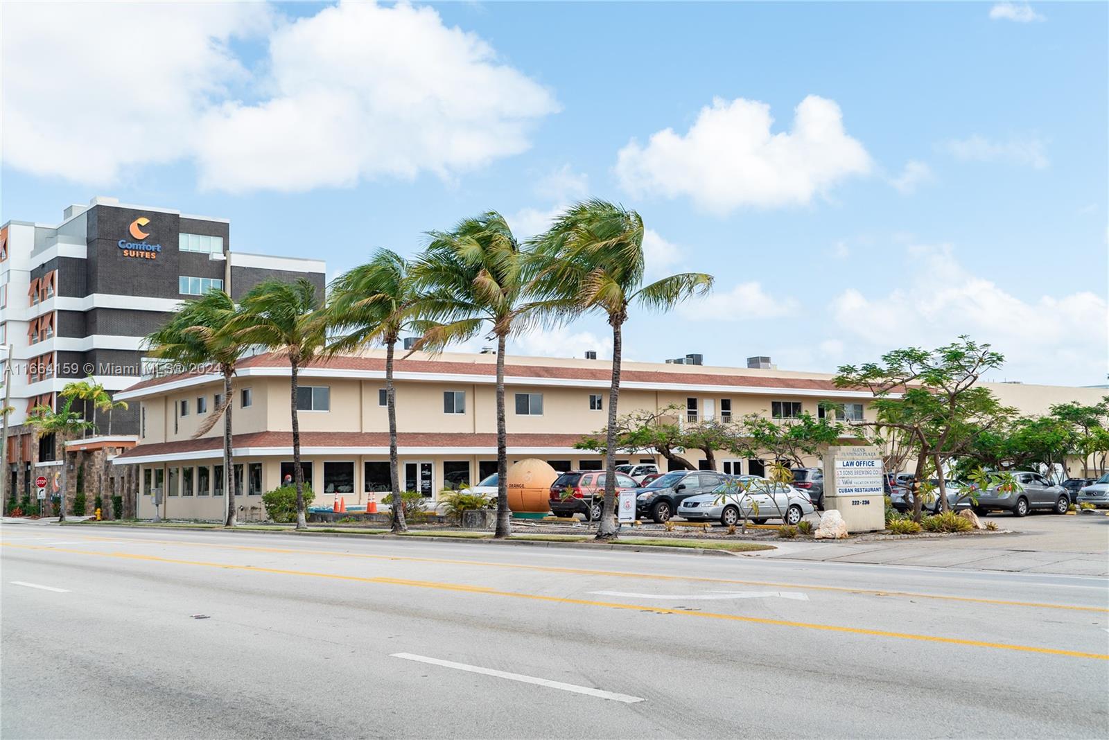 a front view of a building with lot of cars and trees