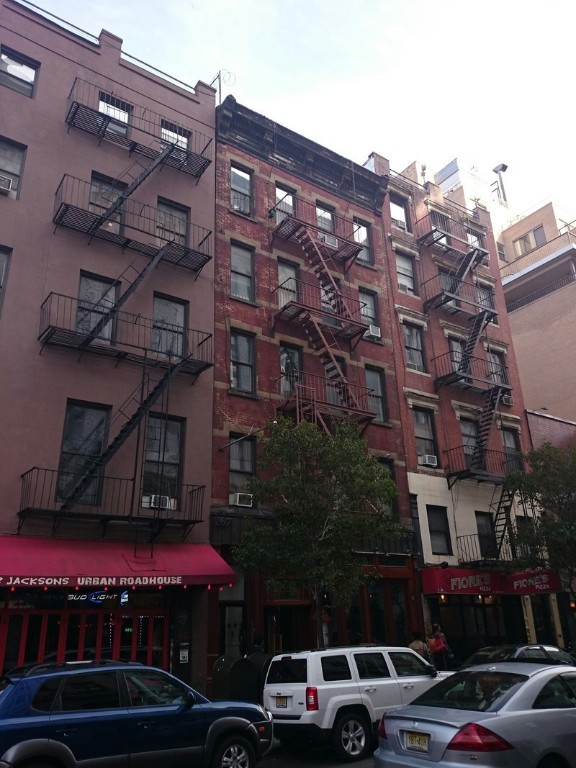 a front view of a building with lot of cars and trees