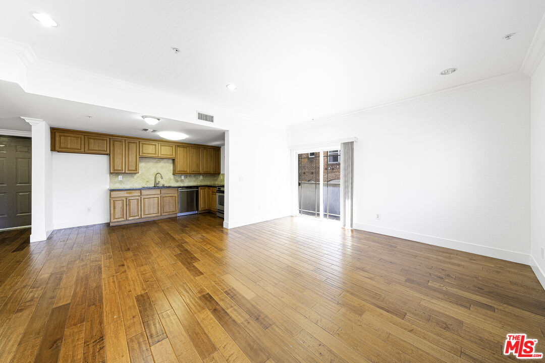 a view of empty room with wooden floor and kitchen