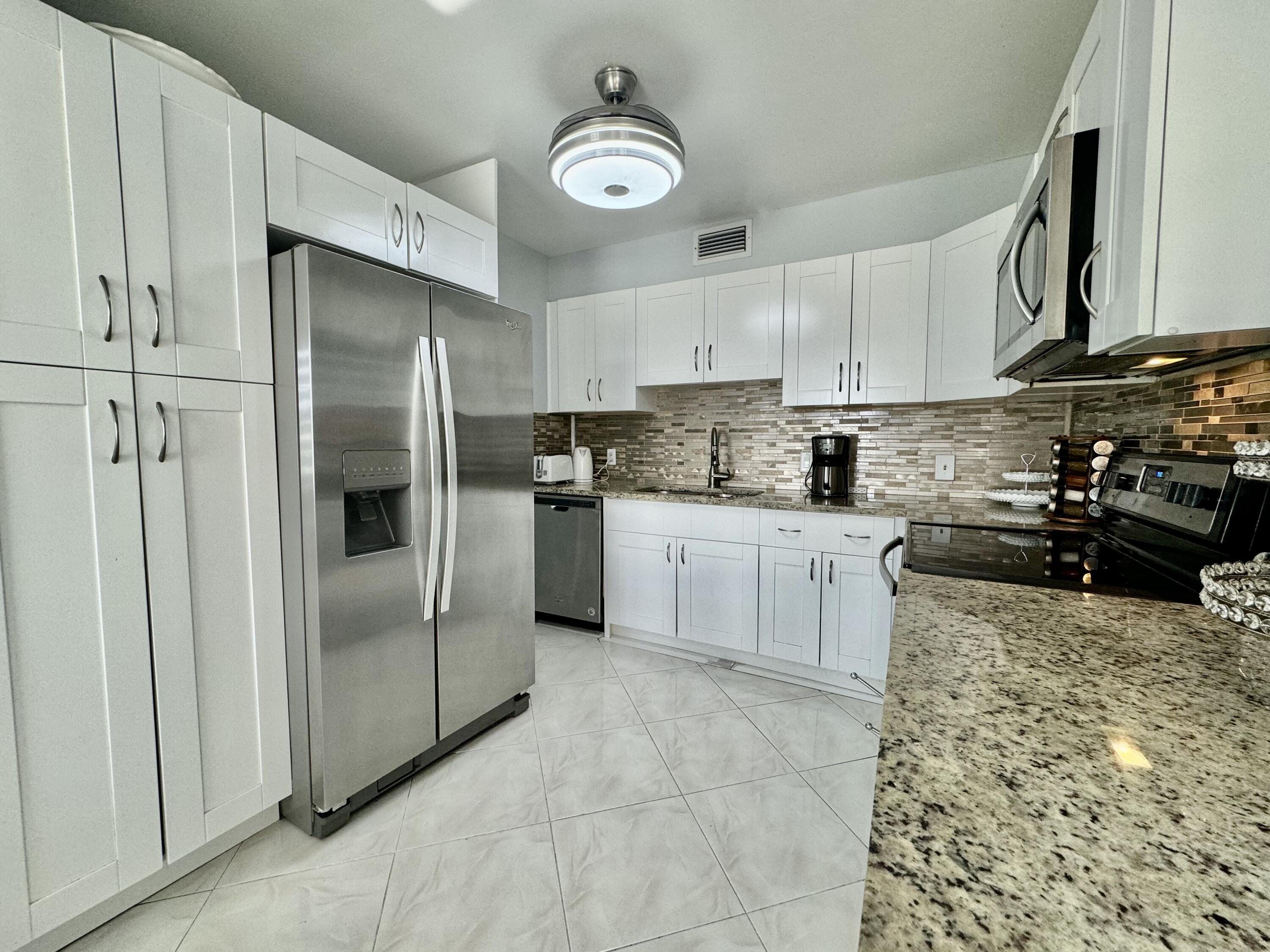 a kitchen with stainless steel appliances granite countertop a refrigerator a stove a sink and white cabinets