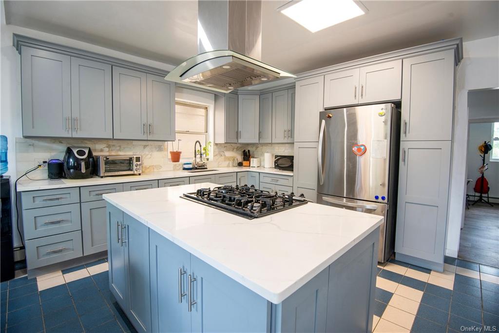 Kitchen featuring island exhaust hood, a kitchen island, stainless steel refrigerator, light tile patterned floors, and gas cooktop