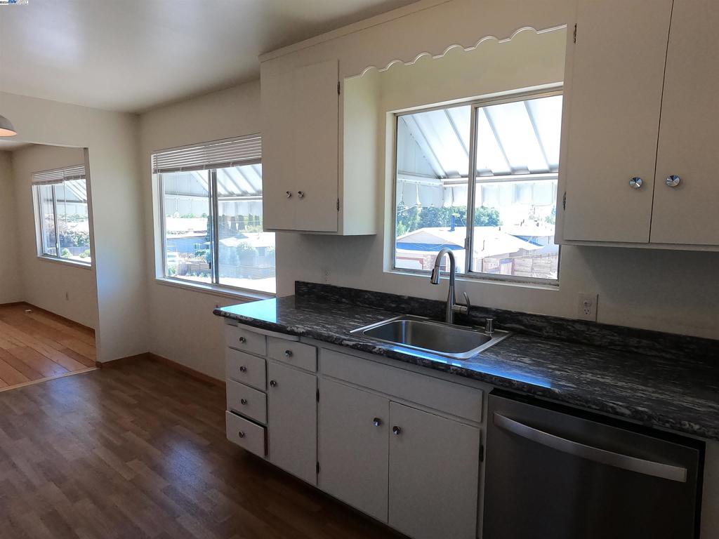 a kitchen with granite countertop wooden floors white cabinets and a window