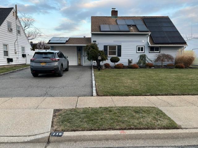 View of front facade featuring a front yard, solar panels, and a garage