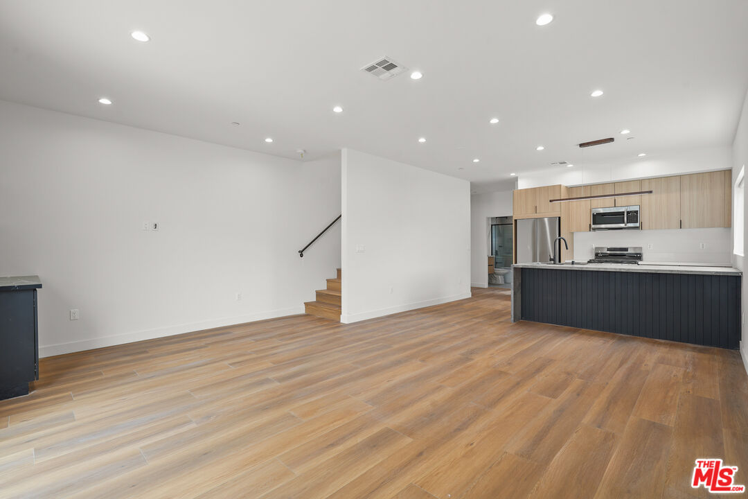a view of an empty room with wooden floor and kitchen