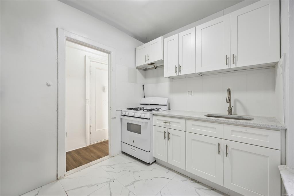 Kitchen with white cabinets, sink, white gas range oven, light hardwood / wood-style flooring, and light stone countertops