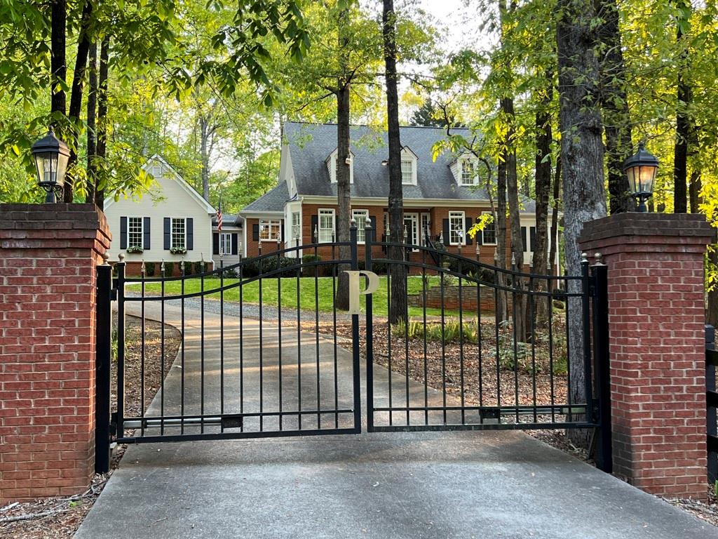 a view of a brick house in front of a yard with plants and large trees