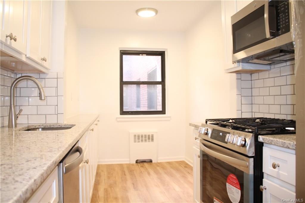 Kitchen with white cabinets, tasteful backsplash, appliances with stainless steel finishes, light stone countertops, and sink