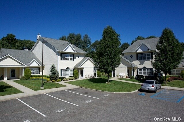 a view of a white house with a big yard plants and large trees