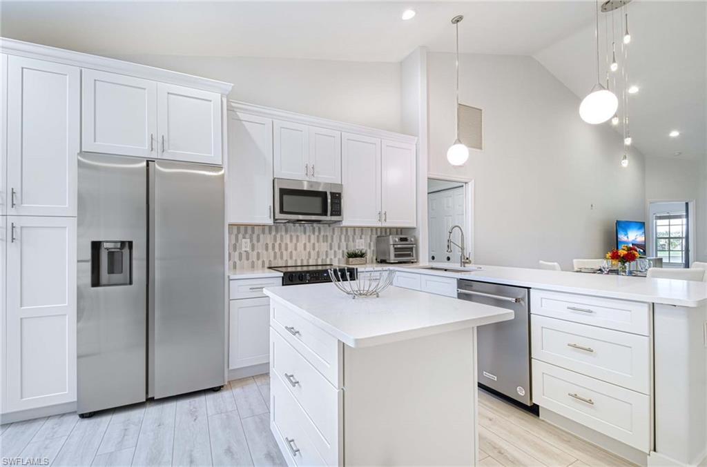 Kitchen with appliances with stainless steel finishes, a kitchen island, white cabinetry, and pendant lighting