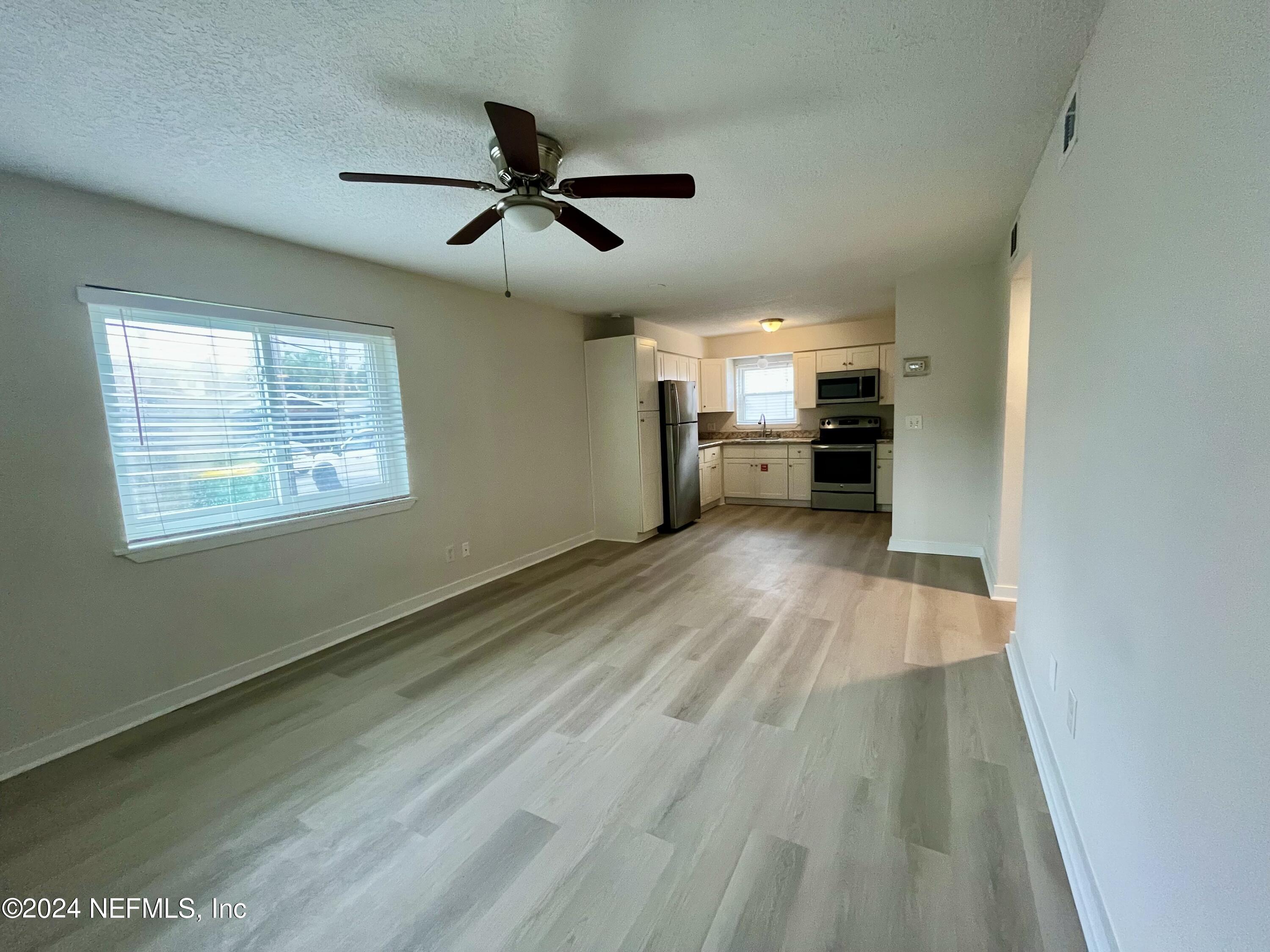 a view of a kitchen with wooden floor a ceiling fan and windows